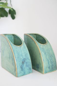 two green vases sitting next to each other on a white counter top with a plant in the background