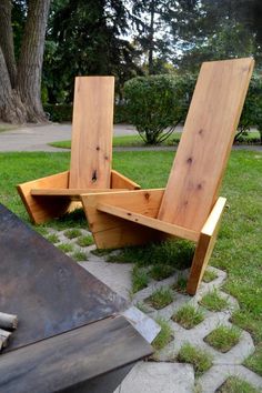 two wooden chairs sitting on top of a grass covered field next to a fire pit