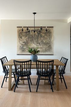 a dining room table with four chairs and a painting on the wall behind it,