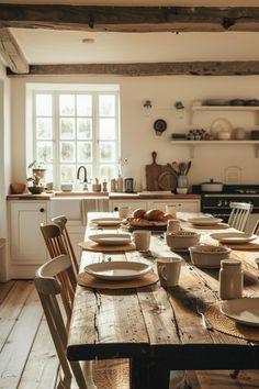 a wooden table topped with white plates and cups next to a stove top oven in a kitchen