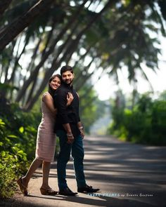 a man and woman standing in the middle of a road surrounded by tall palm trees