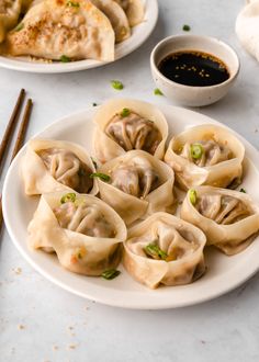 some dumplings are on a white plate with chopsticks and sauce in the background