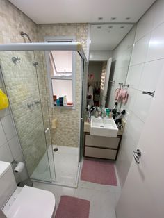 a bathroom with a toilet, sink and shower stall in the corner next to a pink rug on the floor