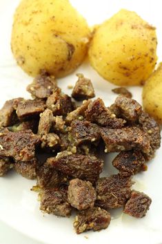 potatoes and meat on a white plate with seasoning sprinkled over them for garnish