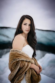 a woman with long hair wearing a white dress and fur stoler standing in the snow