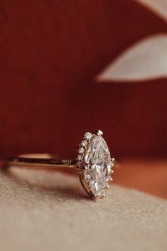 a diamond ring sitting on top of a red velvet surface with a white flower in the background