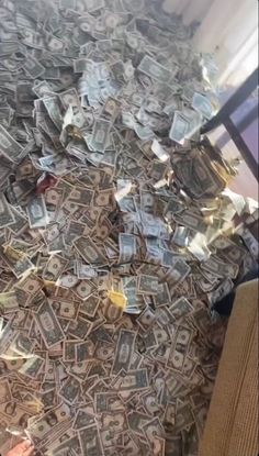 a pile of money sitting on top of a floor next to a metal chair in front of a window