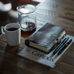 there is a notebook, pen and coffee on the table