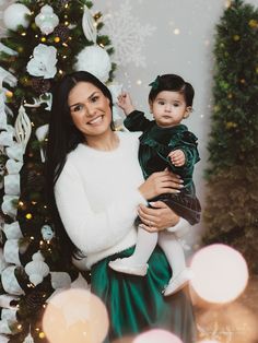 a woman holding a baby in front of a christmas tree