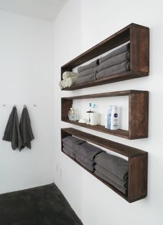 two wooden shelves with towels on them in a white walled bathroom, along with black towel hooks