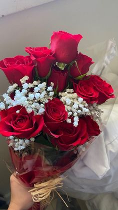 a bouquet of red roses in someone's hand with white baby's breath