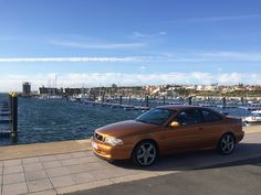 an orange car parked on the side of a road next to a body of water