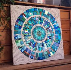 a blue and white mosaic is displayed on a wooden shelf next to a potted plant