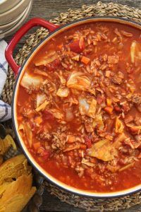 a large pot filled with meat and vegetables next to bread on a wooden table top