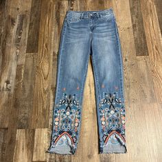 a pair of jeans with embroidered details on the bottom and sides, sitting on a wooden floor