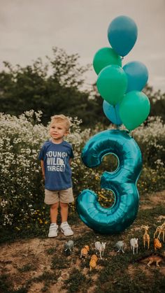 a young boy standing in front of a number 3 balloon with balloons attached to it