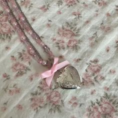 a necklace with a heart shaped pendant and pink ribbon tied around it on a floral fabric