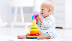 a baby playing with a stacking toy on the floor in a white nursery room