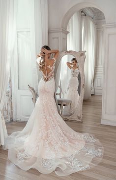 a woman in a wedding dress looking at herself in the mirror with her back to the camera