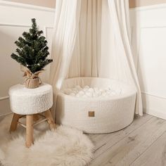 a small christmas tree sits in a white round bed next to a stool and window