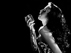 a woman holding a microphone in her right hand and singing into the microphone with both hands