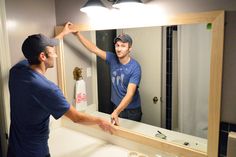 a man standing in front of a bathroom mirror with his hand on the sink's edge