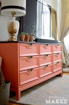 an orange dresser with potted plants on top in front of a mirror and lamp