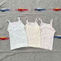 Add a touch of retro charm to your child's wardrobe with this set of three vintage 70s floral tank tops from Sears. Includes one blue, one yellow, and one pink tank top, all crafted from 100% cotton for comfort and breathability. Features: Authentic vintage 1970s design Set of 3: Blue, Yellow, and Pink Made from soft, durable 100% cotton Perfect for size L (6/6x) Measurements: Chest: 22" - 30" Length: 16.5" These tops are ideal for layering or wearing on their own during warm weather. Embrace the timeless floral patterns and vibrant colors that make these tops stand out. Whether for everyday wear or a special occasion, these tank tops are sure to be a favorite. Cute Cotton Camisole For Spring, Cute Fitted Camisole Top, Cute Cotton Tank Camisole, Cute Cotton Sleeveless Camisole, Vintage Sleeveless Cotton Camisole, Cute Floral Print Camisole Top, Cute Cotton Cami Tank Top, Floral Print Cotton Cami Top, Cotton Floral Print Cami Tops