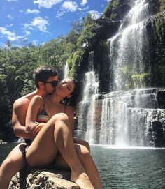 a man and woman sitting next to a waterfall