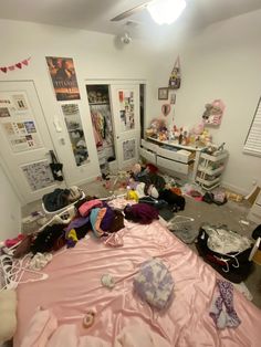 an unmade bed in a cluttered room with lots of stuff on the floor