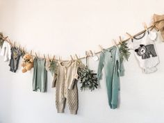 baby clothes hanging on a clothes line with teddy bears and plants next to them in front of a white wall