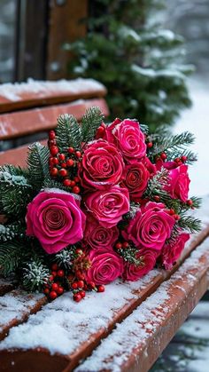 a bouquet of pink roses sitting on top of a wooden bench covered in fresh snow