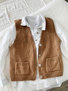 a brown sweater vest sitting on top of a bed next to a white shirt and pillow