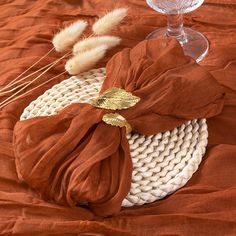 a table topped with an orange cloth and a wine glass next to some dry grass