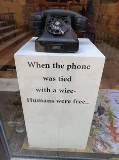 an old phone sitting on top of a sign that says, when the phone was tied with a wire humans were free