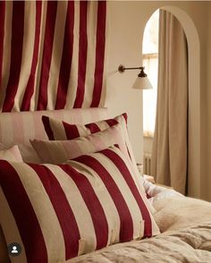 two red and white striped pillows on top of a bed next to an arch window