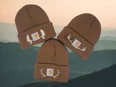 three brown beanies with white deer antlers on them and mountains in the background