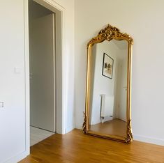 a large gold mirror sitting on top of a hard wood floor next to a doorway