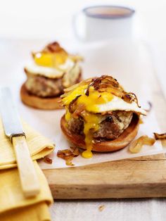 two burgers with eggs and bacon on a cutting board