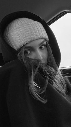 a woman sitting in the back seat of a car wearing a white hat and black coat