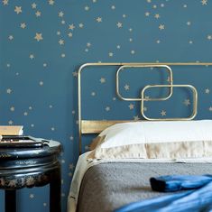 a bed with blue and gold stars on the wall next to a night stand in a bedroom