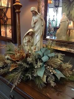 a christmas arrangement on top of a dresser with a statue and mirror in the background