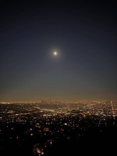 the city lights are lit up in the night sky as the moon shines overhead