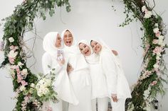 four women standing in front of a floral arch with their arms around each other and laughing