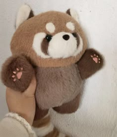 a hand holding a brown and white stuffed animal with paws on it's face