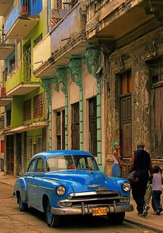 an old blue car is parked on the side of the road in front of some buildings