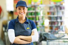 a woman in an apron and hat is standing with her arms crossed, smiling at the camera