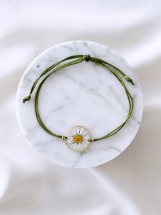 a white marble plate topped with a green string bracelet and a yellow bead charm