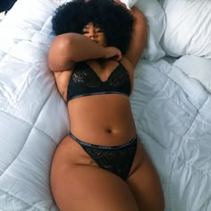 a woman laying on top of a bed in a black bra and panties with her arms behind her head