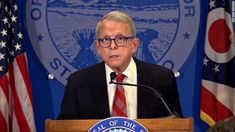 a man standing at a podium in front of flags